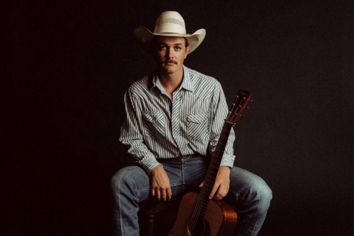 Country musician with guitar, cowboy hat, casual denim, and striped shirt for authentic country vibe.
