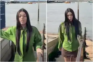 Woman in green jacket standing near water at the seaside.