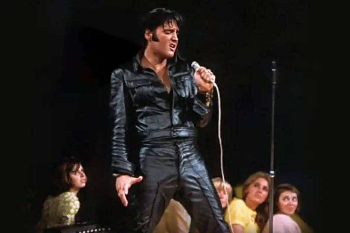 Elvis Presley singing into a microphone on stage with backup singers.
